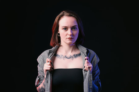Young woman with piercings, tattoos and stylish clothes on black backgroundの写真素材