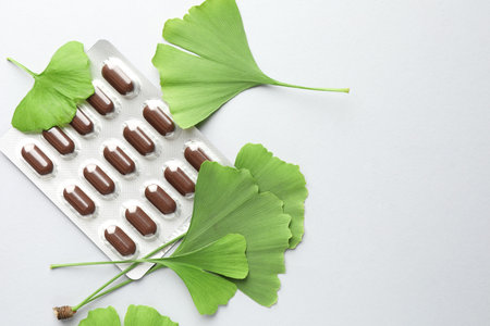 Ginkgo biloba leaves and blister of pills on light gray background, flat lay. Space for textの写真素材