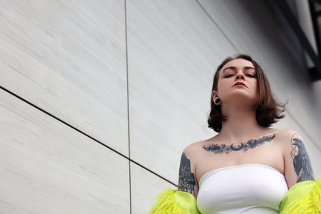 Young woman with piercings, tattoos and stylish clothes outdoors, low angle view. Space for textの写真素材