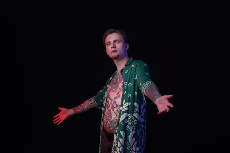 Young man with piercings, tattoos and stylish clothes posing on black background