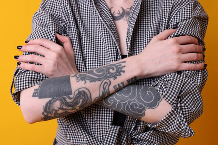 Young woman with tattoos and stylish clothes posing on yellow background, closeup
