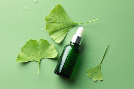 Wet ginkgo biloba leaves and bottle of essential oil on green background, flat layの写真素材