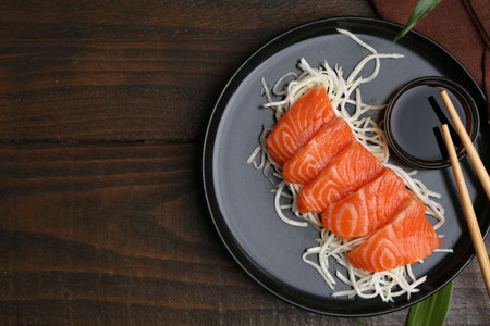 Fresh salmon sashimi with sliced radish, soy sauce and chopsticks on wooden table, flat lay. Space for textの写真素材