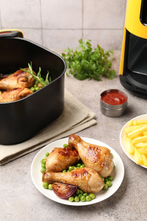 Air fryer with grilled chicken drumsticks and French fries on gray tableの写真素材