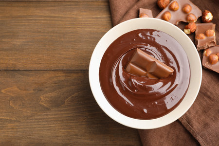 Melted chocolate and pieces with hazelnuts on wooden table, flat lay. Space for textの写真素材