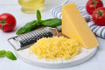Grated cheese, grater and products on white tiled table, closeupの写真素材