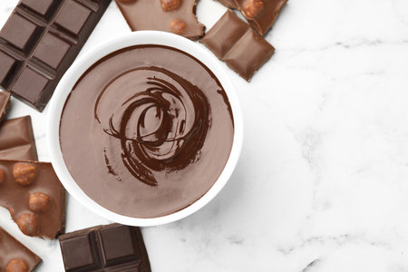 Bowl with melted chocolate and pieces on white marble table, flat lay. Space for textの写真素材