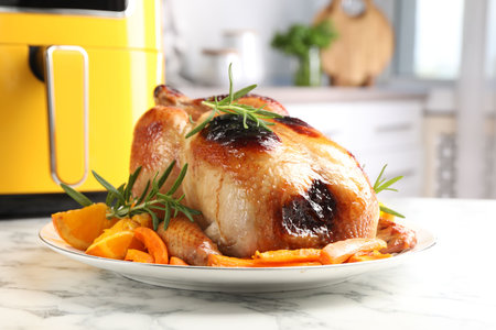 Tasty grilled chicken with rosemary, vegetables and air fryer on white marble table, closeupの写真素材