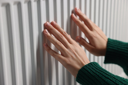 Woman warming her hands near radiator indoors, closeupの写真素材