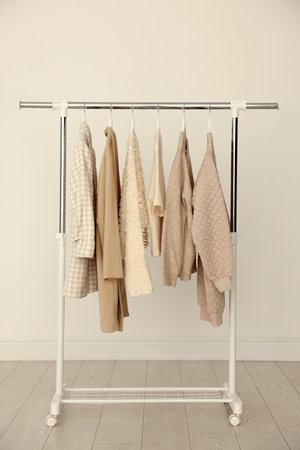 Different clothes hanging on rack near light wallの写真素材