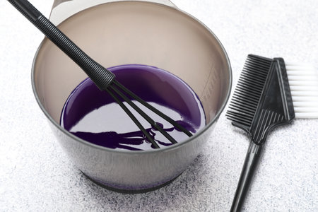 Hair dyeing product in bowl and hairdresser's tools on light gray table, closeupの写真素材
