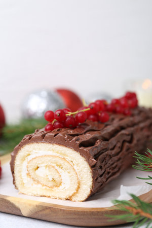 Delicious Yule log (traditional Christmas cake) with redcurrant and fir tree branches on light table, closeupの写真素材