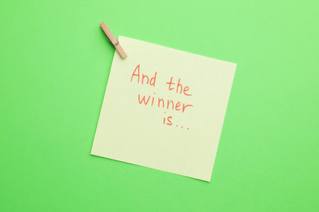 Sticky note with phrase And The Winner Is on green background, top viewの写真素材
