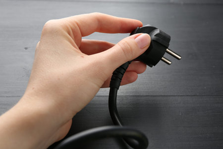 Woman holding plug at black wooden table, closeup