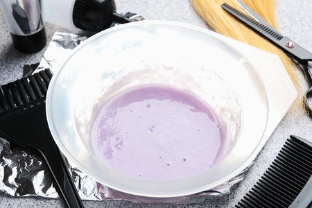 Hair dyeing product in bowl, lock of hair and different hairdresser's tools on light gray table, closeupの写真素材