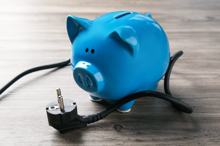 Electrical wire with plug and piggy bank on wooden table, closeup