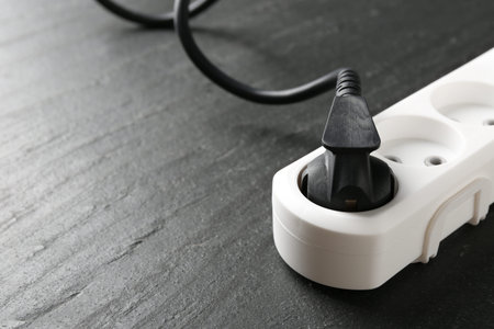 Power strip with electrical plug on black table, closeup. Space for text