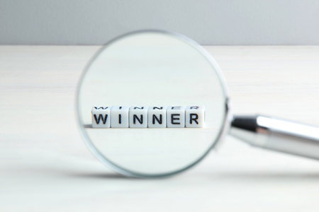 Word Winner made of cubes on white wooden table, view through magnifying glassの写真素材