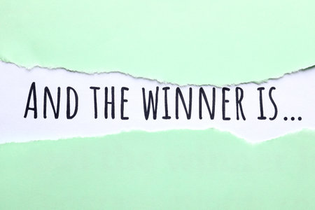 Phrase And The Winner Is on white background, view through hole in torn pale green paperの写真素材