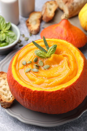 Tasty pumpkin cream soup with seeds and basil served in pumpkin on gray table, closeupの写真素材