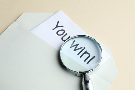 Paper note with phrase You Win! in envelope and magnifying glass on beige background, closeupの写真素材