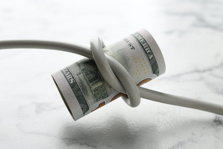 Electrical wire with banknote on white marble table, closeup