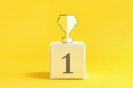 Paper trophy cup on cube number 1 against yellow backgroundの写真素材