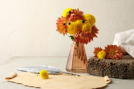 Autumn composition with flowers in vase and old paper on light gray table, space for textの写真素材