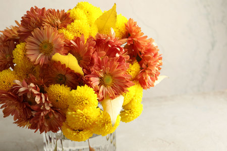 Autumn atmosphere. Vase with beautiful flowers and leaves on light gray table, closeup. Space for textの写真素材
