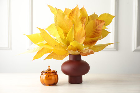 Autumn atmosphere. Vase with beautiful dry leaves and candle on white wooden tableの写真素材