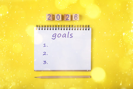 New 2026 Year Goals. Inscription in notebook and cubes with numbers on yellow background, top view. Bokeh lightsの写真素材