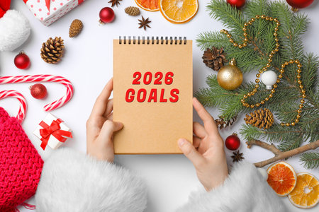 New 2026 Year Goals. Woman holding notebook at table with festive stuff, top view