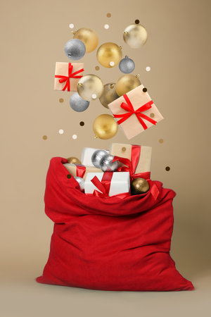 Christmas balls and gift boxes falling into red Santa bag on dark beige backgroundの写真素材