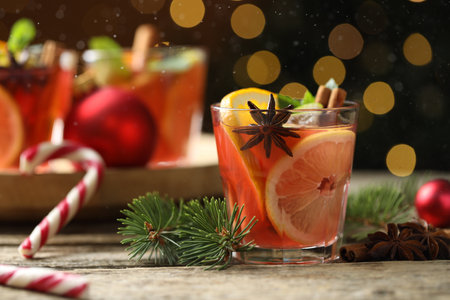 Tasty punch drink in glass, spices and Christmas decor on wooden table against background with blurred lights, closeup. Bokeh effectの写真素材
