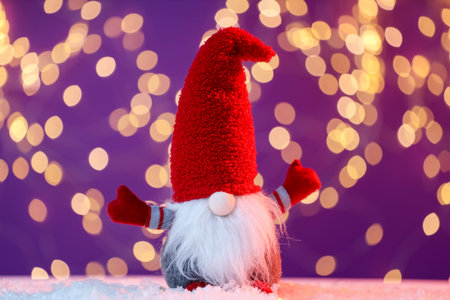 Funny Christmas gnome on artificial snow against purple background with blurred lights. Bokeh effectの写真素材