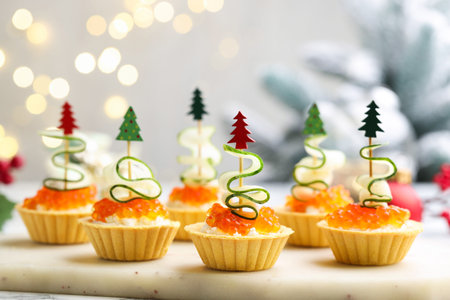 Christmas food. Tasty tartlets with red caviar, cream cheese, cucumber and decor on table against background with blurred lights, closeup. Bokeh effectの写真素材