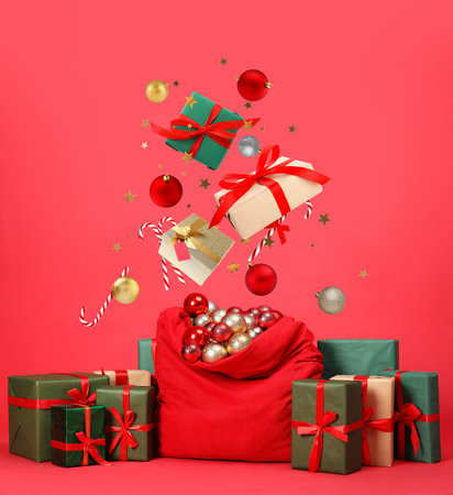 Christmas balls, gift boxes, candy canes and confetti falling into bag on red backgroundの写真素材
