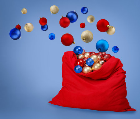 Christmas balls falling into red Santa bag on blue backgroundの写真素材