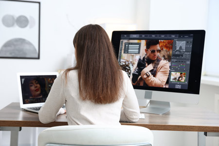 Professional retoucher editing photo on computer and laptop at table in office, back view