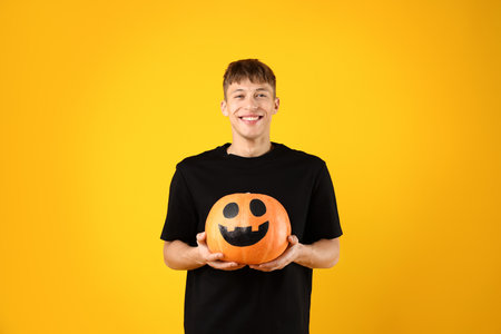 Halloween celebration. Man holding pumpkin with drawn face on orange backgroundの写真素材