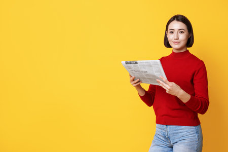 Beautiful woman with newspaper against yellow background. Space for textの写真素材