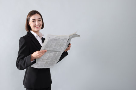 Portrait of smiling woman in suit with newspaper on gray background. Space for textの写真素材