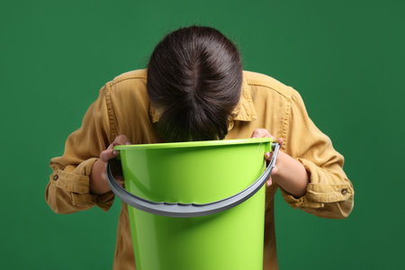 Young woman with bucket suffering from nausea on green backgroundの写真素材
