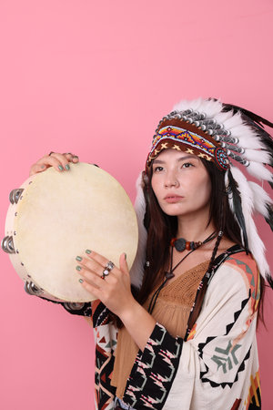 Shaman woman in native American Indian headdress with tambourine on pink backgroundの写真素材