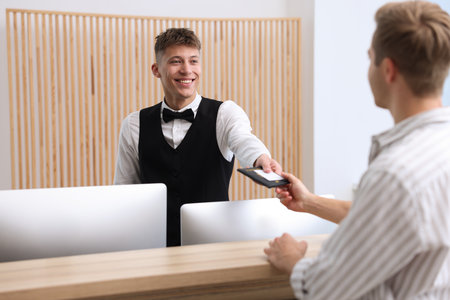 Receptionist giving passport and hotel key card to guest at reception desk indoorsの写真素材