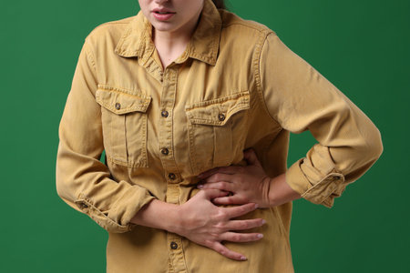 Young woman suffering from stomachache and nausea on green background, closeup