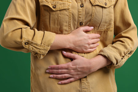 Young woman suffering from stomachache and nausea on green background, closeupの写真素材