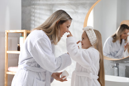 Mother and daughter applying cream on each others faces in bathroomの写真素材