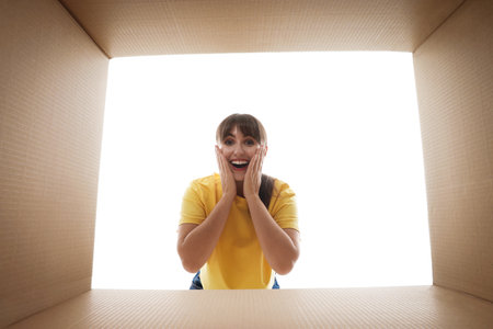 Woman looking into cardboard box against white background, view from inside packageの写真素材