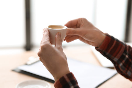 Woman having coffee break at wooden desk indoors, closeupの写真素材